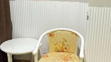 Una silla blanca con un cojín estampado y una mesita blanca a su lado.