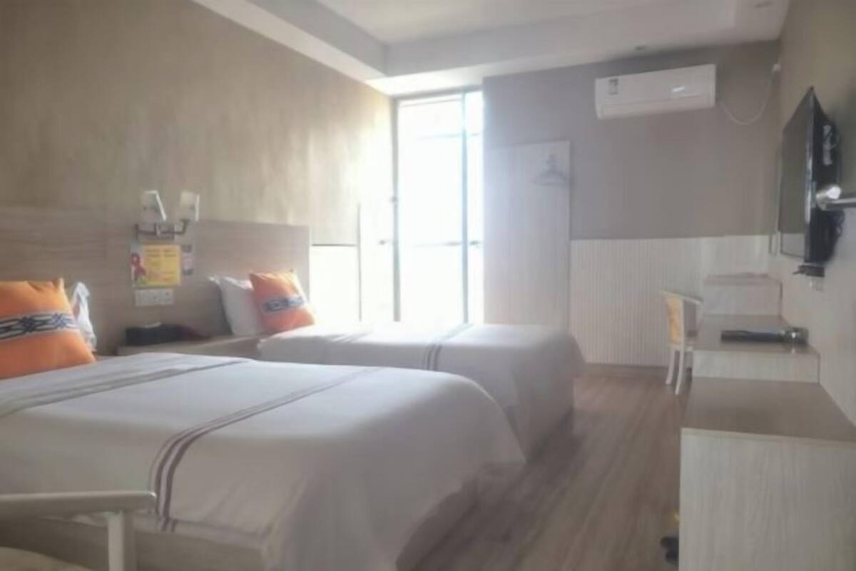 A hotel room with two beds, a desk, a chair, a TV, and a window.