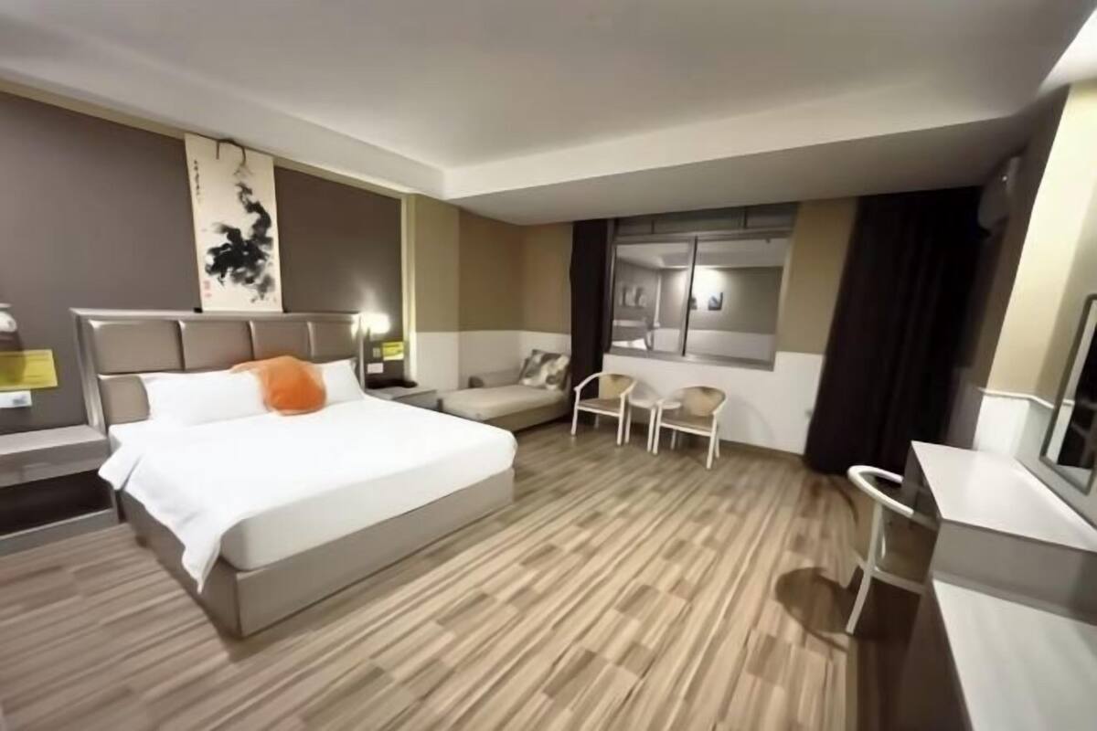 A hotel room with a bed, a desk, a chair, a sofa, and a large mirror.
