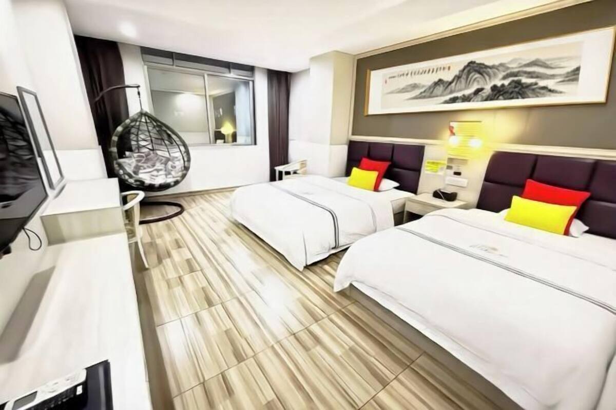 A hotel room with two beds, a desk, a chair, a television, and a window with a view.