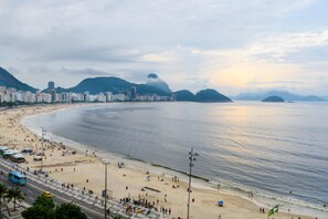 A beach with a cityscape in the background, including buildings and mountains.