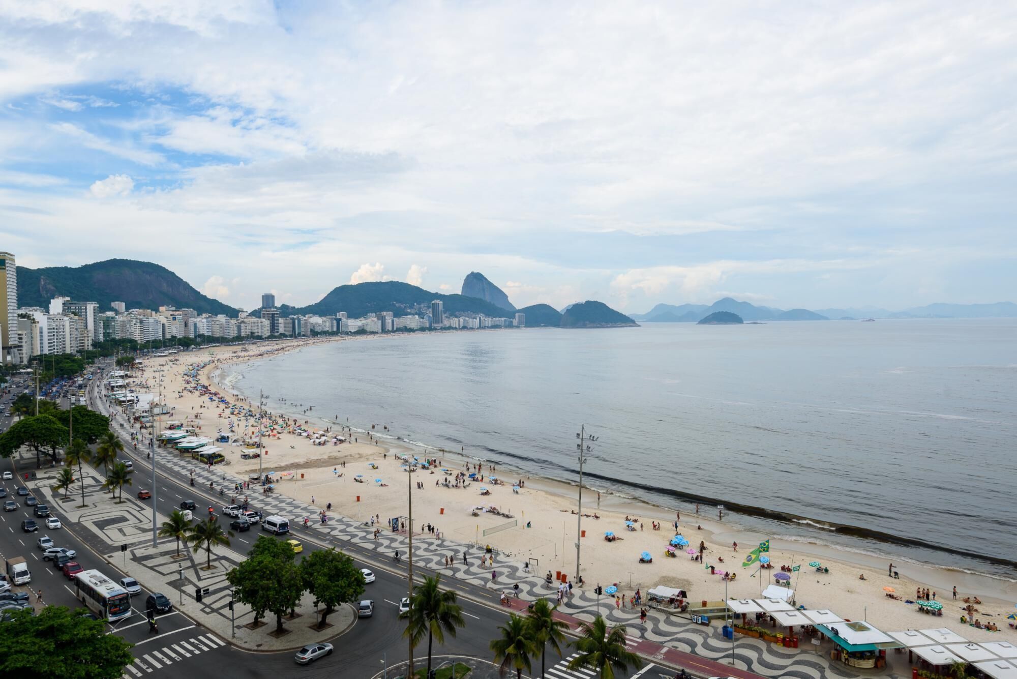 Una playa con una costa curva, palmeras y un paisaje urbano al fondo.