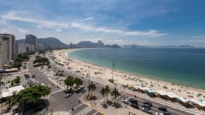 A coastal cityscape with a wide beach, clear blue sky, and urban buildings. - View of Copacabana Beach A1103 (Rio de Janeiro)