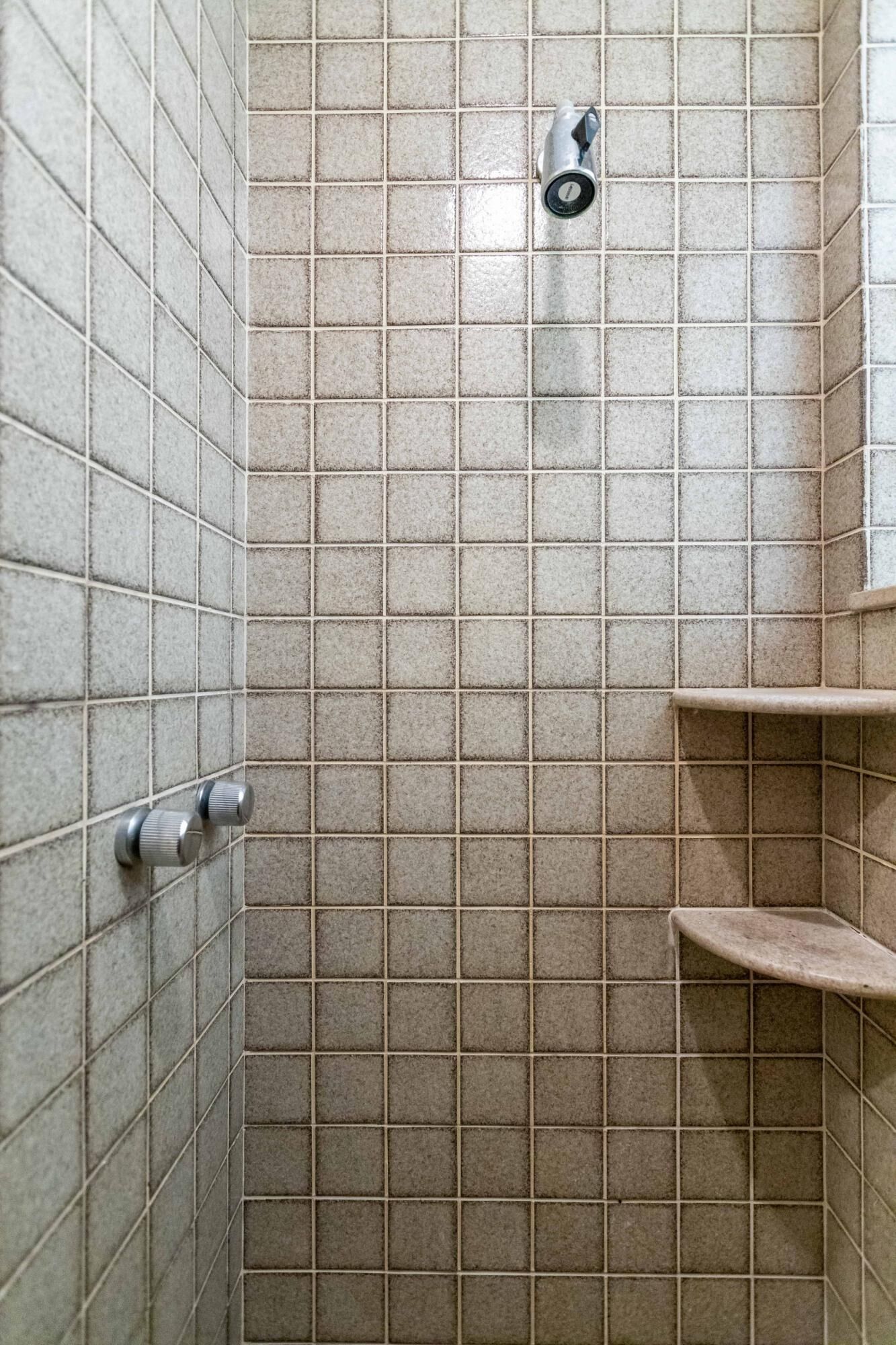 Une zone de douche carrelée, dotée d’un panneau de commande et d’une étagère.