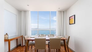 A dining area with a view of the sea, a wooden table set for six, and a painting on the wall. - View of Copacabana Beach A1103 (Rio de Janeiro)