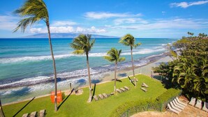 A beach view with palm trees, a grassy area with lounge chairs, and a clear blue sky. - The Paradise Penthouse (Lahaina)