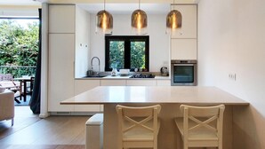 A modern kitchen with a large island, pendant lights, and a view of greenery outside. - Dizengoff Brique in Tel Aviv-yafo (Tel Aviv)
