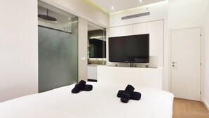 A modern bedroom with a large bed, a flat-screen TV mounted above it, and a sliding glass door leading to a bathroom. - Dizengoff Brique in Tel Aviv-yafo (Tel Aviv)
