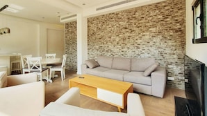 A modern living room with a grey sofa, white chairs, a wooden coffee table, and a stone wall. - Dizengoff Brique in Tel Aviv-yafo (Tel Aviv)