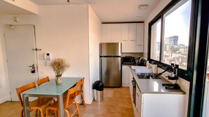 A compact kitchen with a stainless steel refrigerator, a sink, and a window overlooking a cityscape. - Kalisher Ophrys in Tel Aviv-yafo (Tel Aviv)