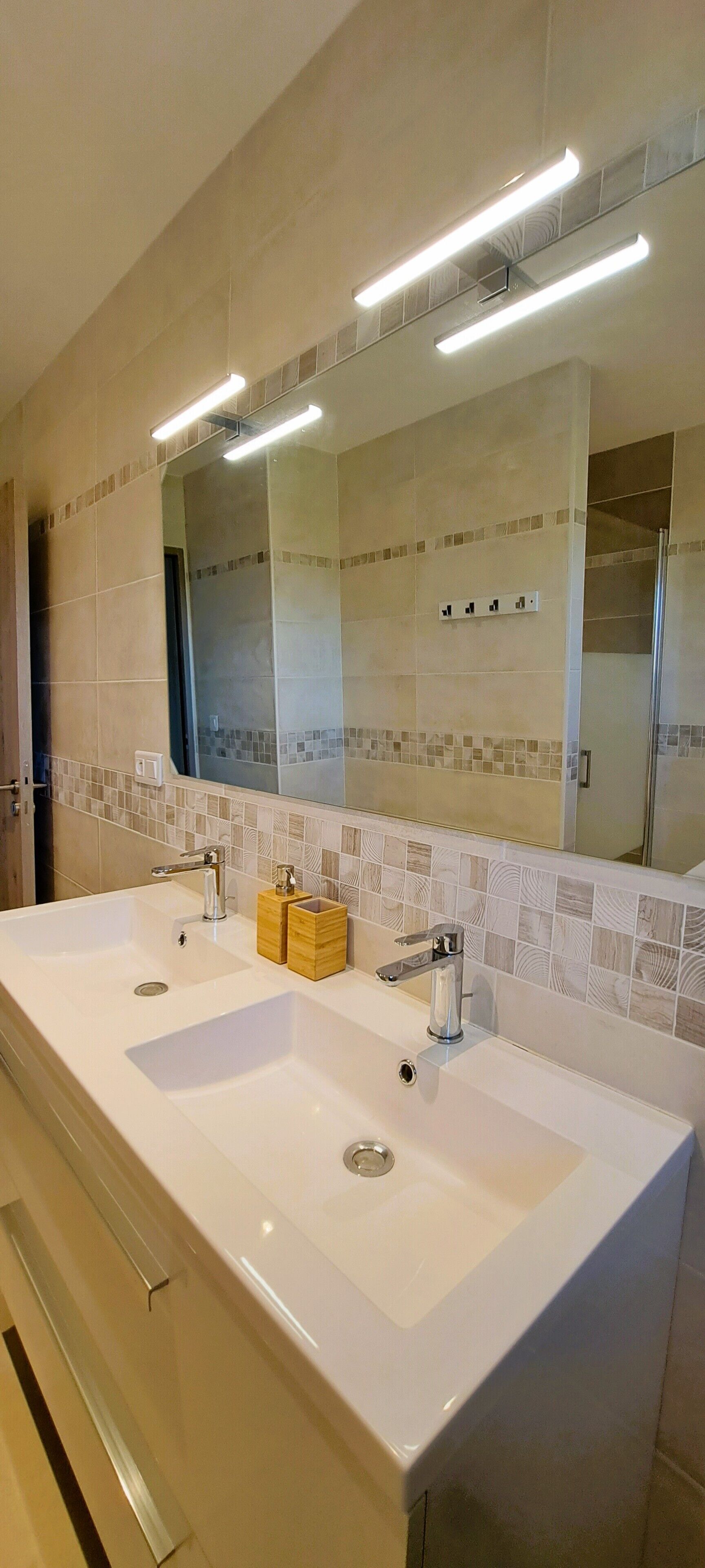 Casa de banho com duas pias, um espelho grande e painel de azulejos.