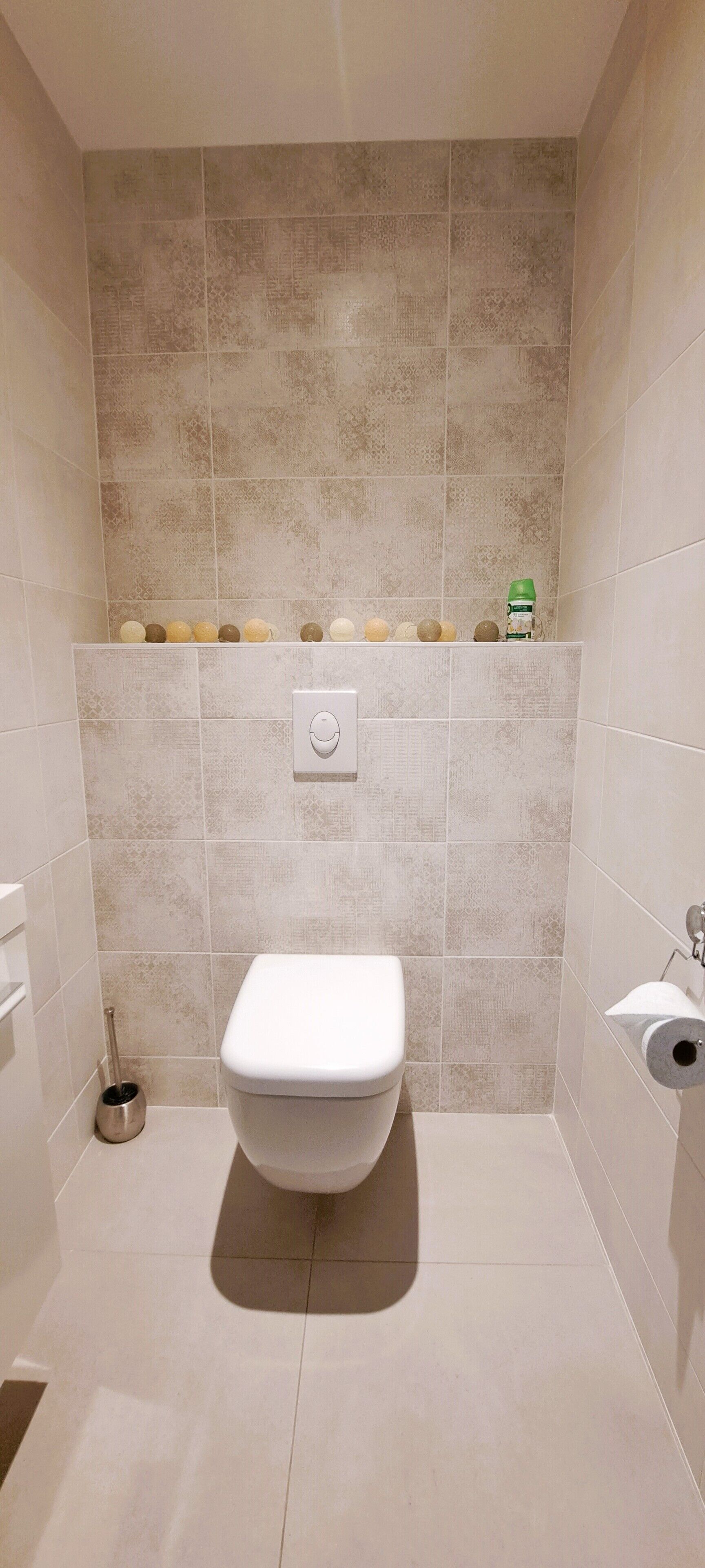 Ein kleines, modernes Badezimmer mit Toilette, einem Händetrockner und Ablageflächen für Toilettenartikel.