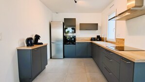 Una cuina moderna amb armaris grisos, un refrigerador d'acer inoxidable, un forn encastrat i un taulell de fusta.
