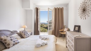 Un dormitorio con cama, cómoda, silla, lámpara y vistas al exterior.