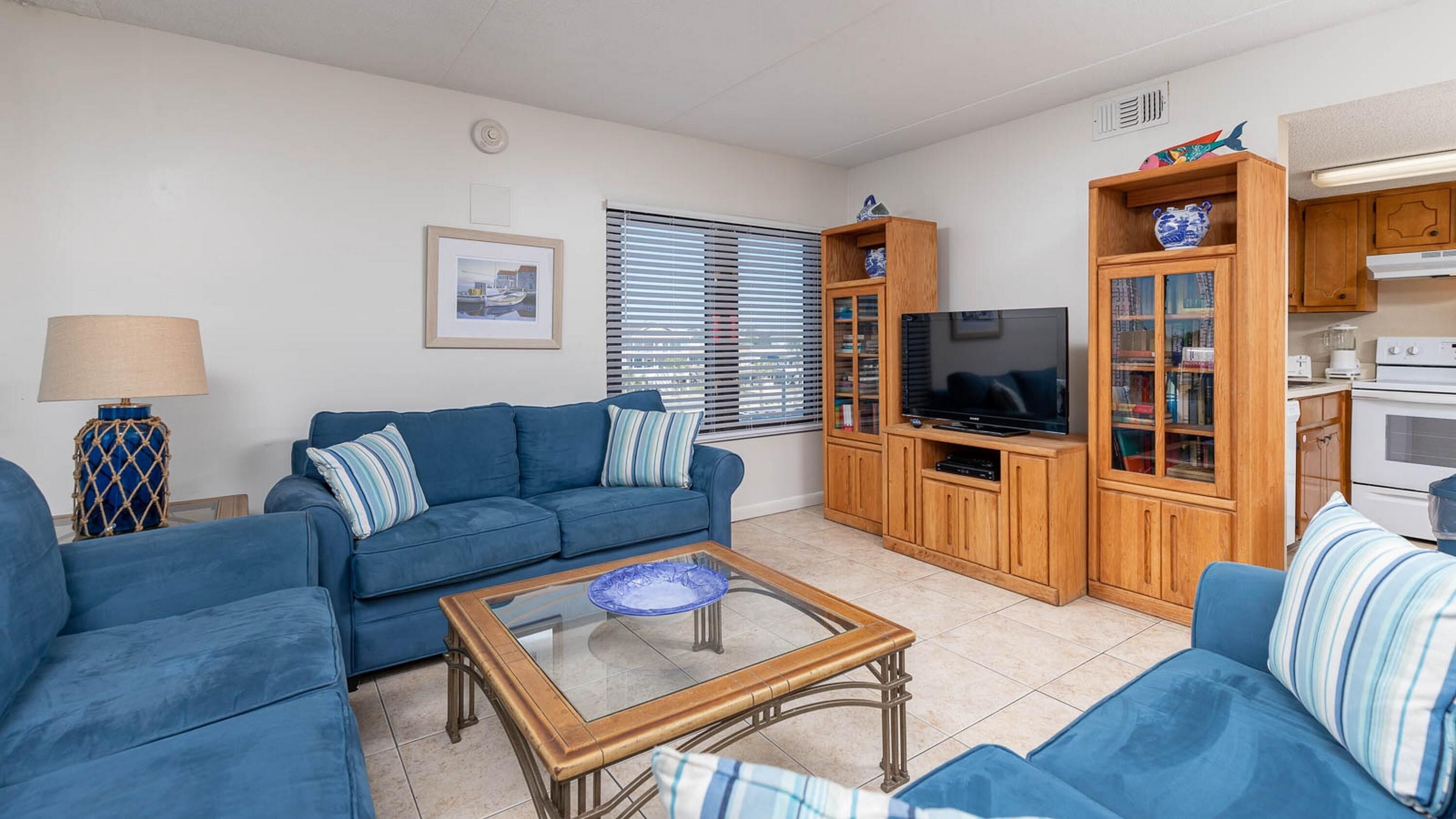 A living room with a blue sofa, a coffee table, a TV, and wooden cabinets.