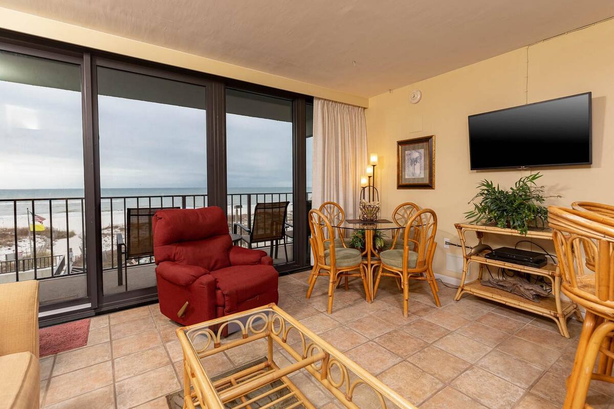 Ein Balkon mit einem roten Stuhl, Korbstühlen, einem Tisch und einem Fernseher.