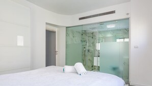 Ein modernes Hotelzimmer mit einem großen Bett, einer Duschkabine aus Glas und einem weißen Kleiderschrank.