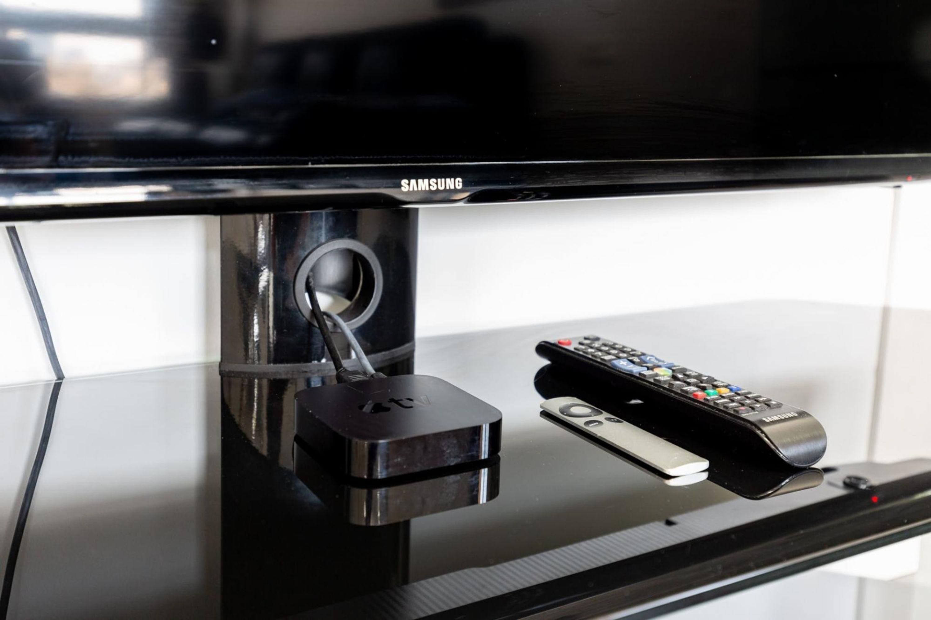 Ein an einer Wand befestigter Samsung Fernseher mit Fernbedienung und Kabelanschlussbox auf dem Fuß.