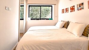 A bedroom with a large bed, a window with blinds, and a wall with several framed pictures. - Rupin Nacre in Tel Aviv-yafo (Tel Aviv)