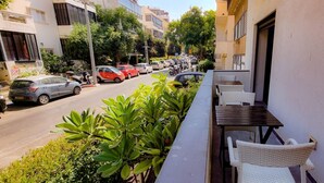 A balcony with a table and chairs, overlooking a street with parked cars and buildings. - Rupin Nacre in Tel Aviv-yafo (Tel Aviv)