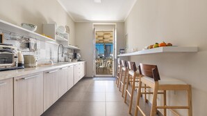 A modern kitchen with a long countertop, wooden chairs, and a view to the dining area. - 2674 B&B Albatro - Camera Tripla (Taviano)