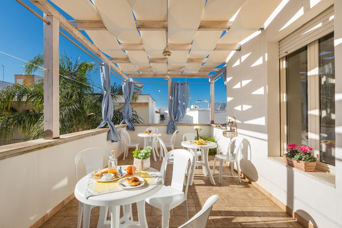 La terrazza di Albatro B&B con pergola bianca, tavolini apparecchiati per la colazione e piante