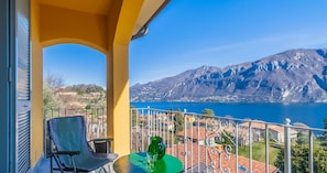A balcony with a table, a chair, and a view of a lake and mountains.