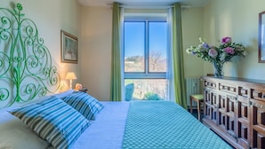 Un dormitorio con cama, mesita de noche, cómoda, ventana con cortinas y cabecera decorativa verde.