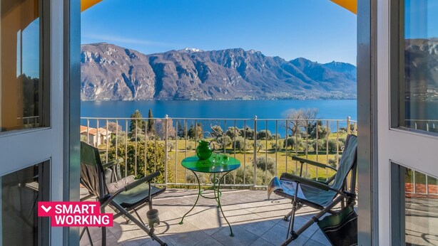 Un balcón con una mesa, sillas y vistas a montañas y un lago.