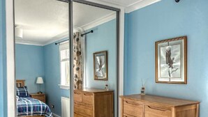 A bedroom with a large sliding door leading to another room, a wooden dresser, and two framed pictures on the wall. - Comfy house in West Lothian - 10 min from the airport! (Broxburn)
