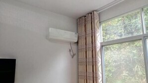 A room with a large window, a wall-mounted air conditioner, and a curtain.
