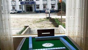 A room with a green pool table, a window overlooking a street with a police station and parked cars.