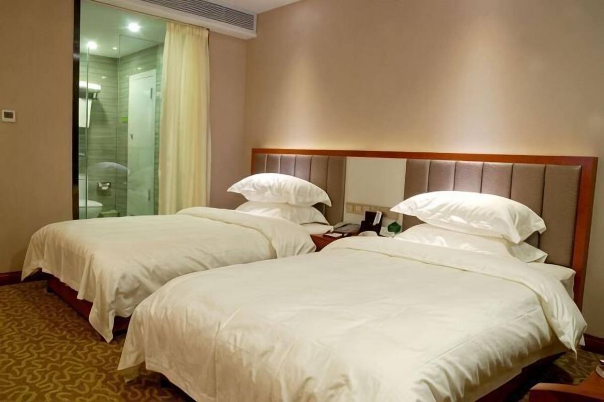A hotel room with two beds, a shower, and a bathroom with a glass door.