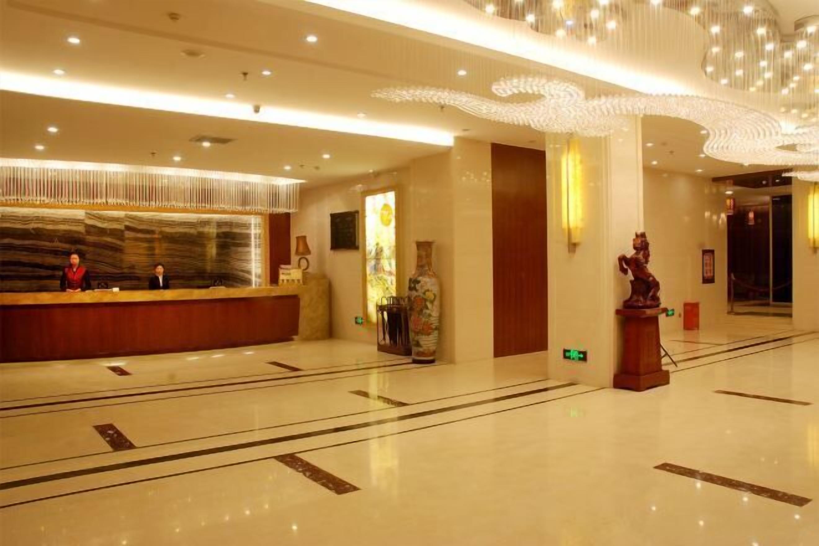 Un vestíbulo de hotel con mostrador de recepción, un cuadro abstracto de gran tamaño, una estatua y un suelo de mármol pulido.