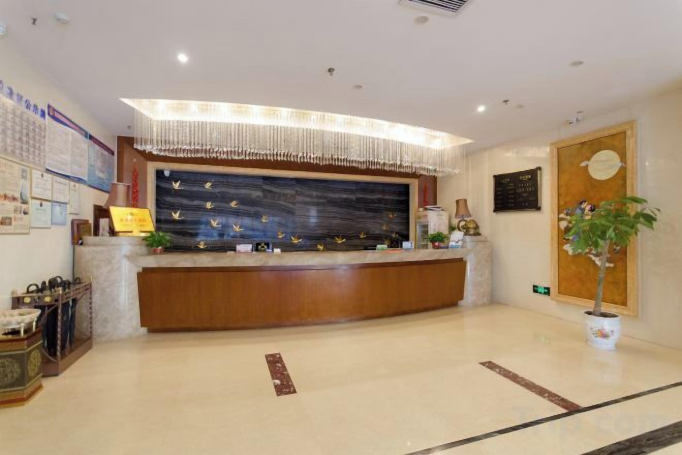 A hotel reception area with a wooden reception desk, a wall-mounted clock, and a potted plant.