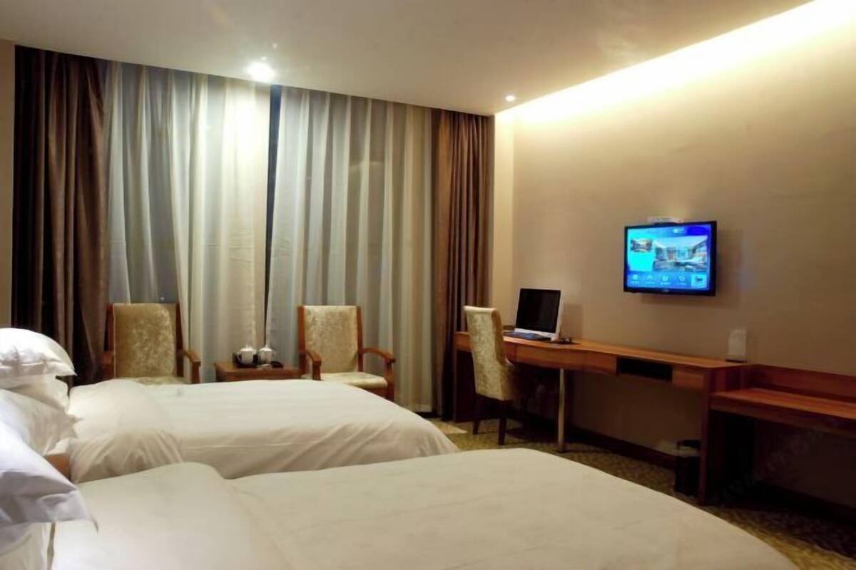 A hotel room with two beds, a desk, a chair, a television, and curtains.