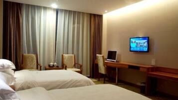 Quarto de hotel com duas camas, uma escrivaninha, uma cadeira e uma televisão na parede.