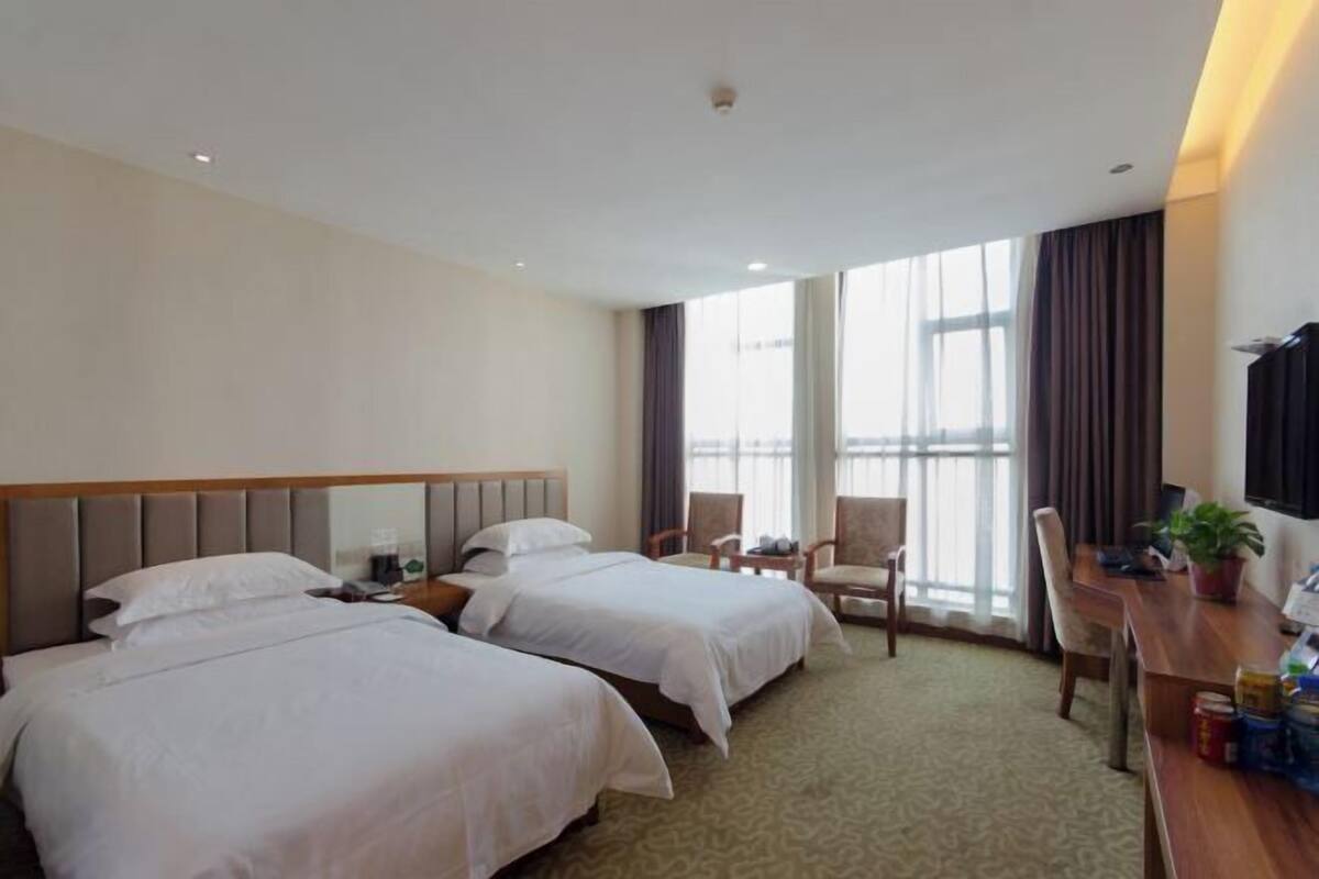 A hotel room with two beds, a desk, chairs, and large windows.