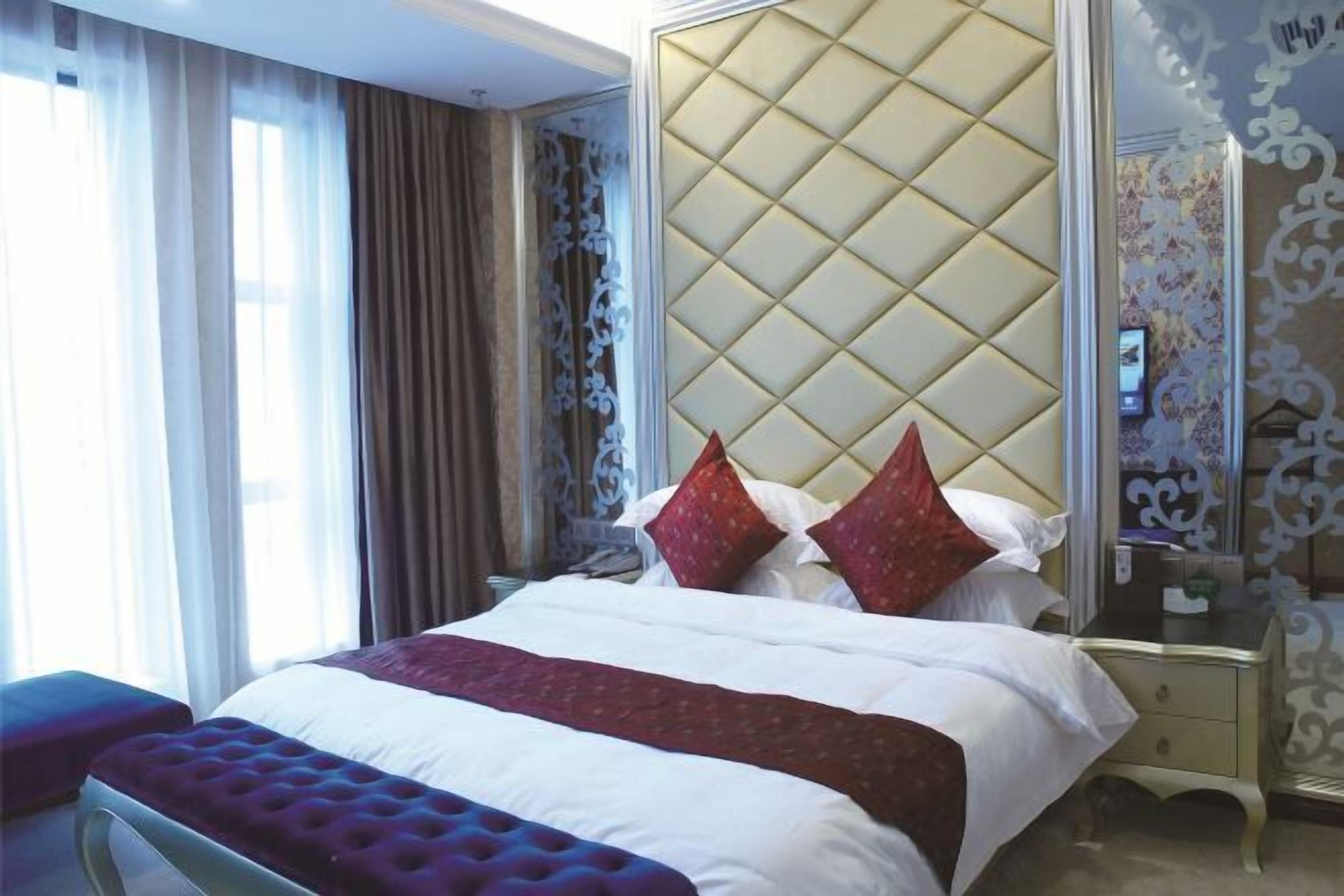 A hotel room with a large bed, a nightstand, a dresser, and a mirror.