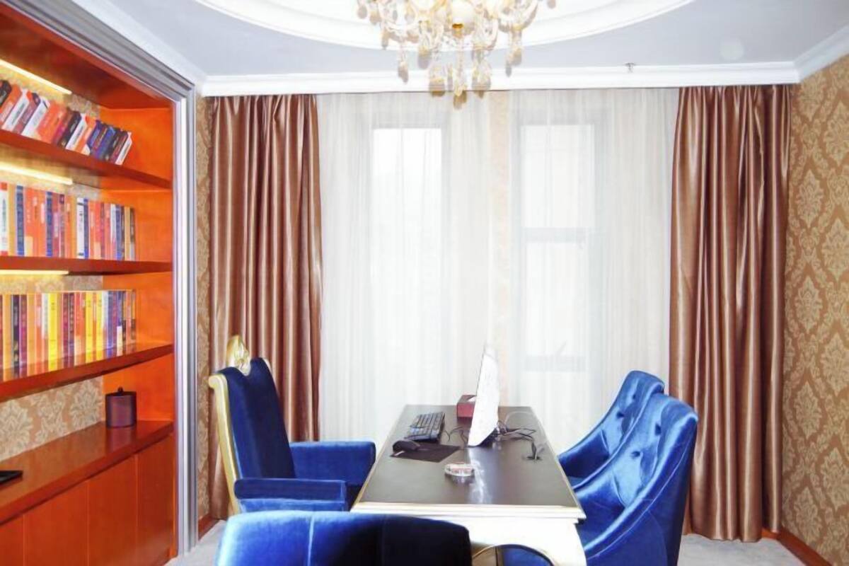 A room with a wooden bookshelf, a table with chairs, and a chandelier.