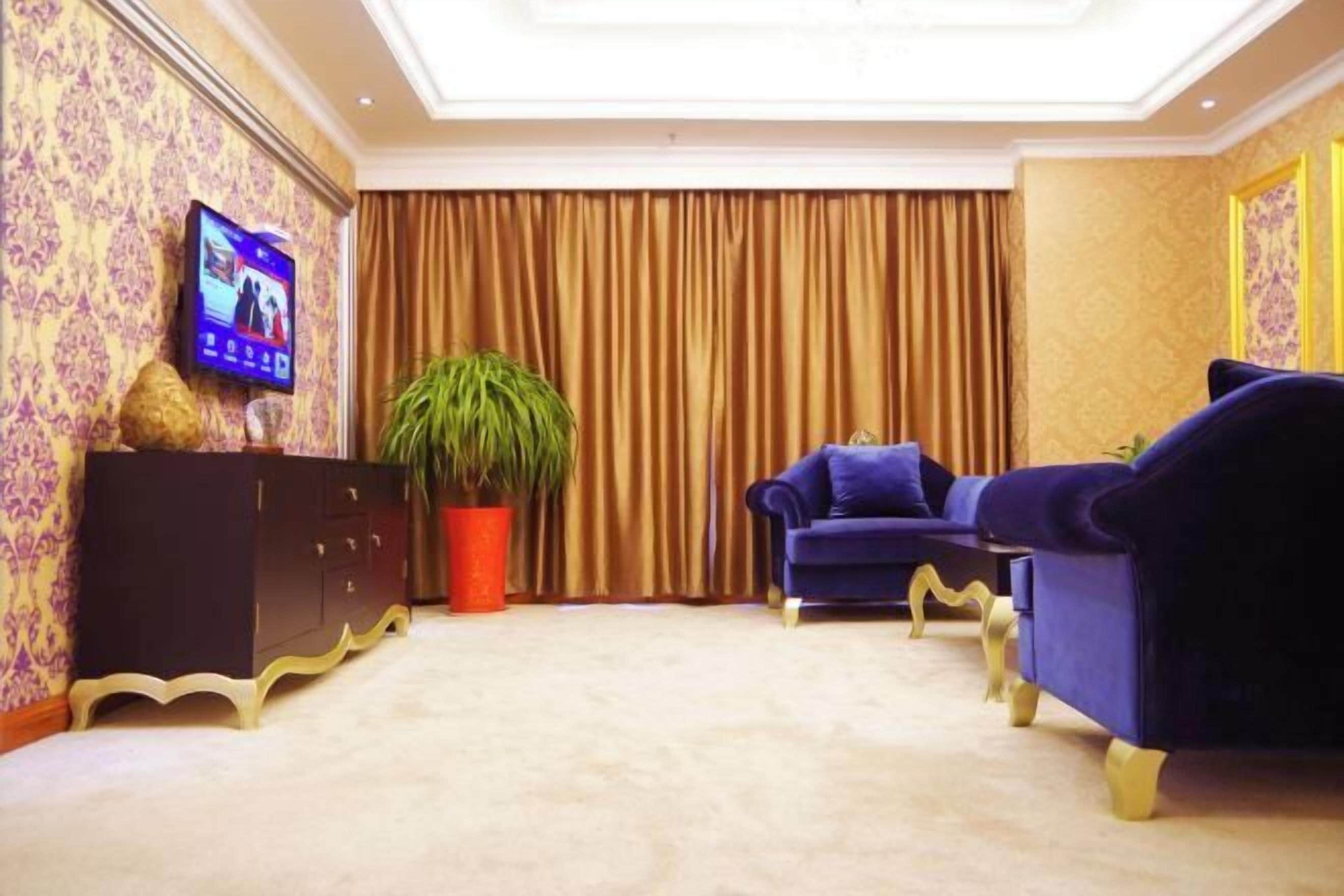 Una habitación con televisor, una planta grande en maceta, un sofá azul y un mueble de color oscuro.