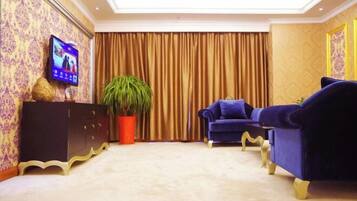 Una habitación con televisor, una planta grande en maceta, un sofá azul y un mueble de color oscuro.