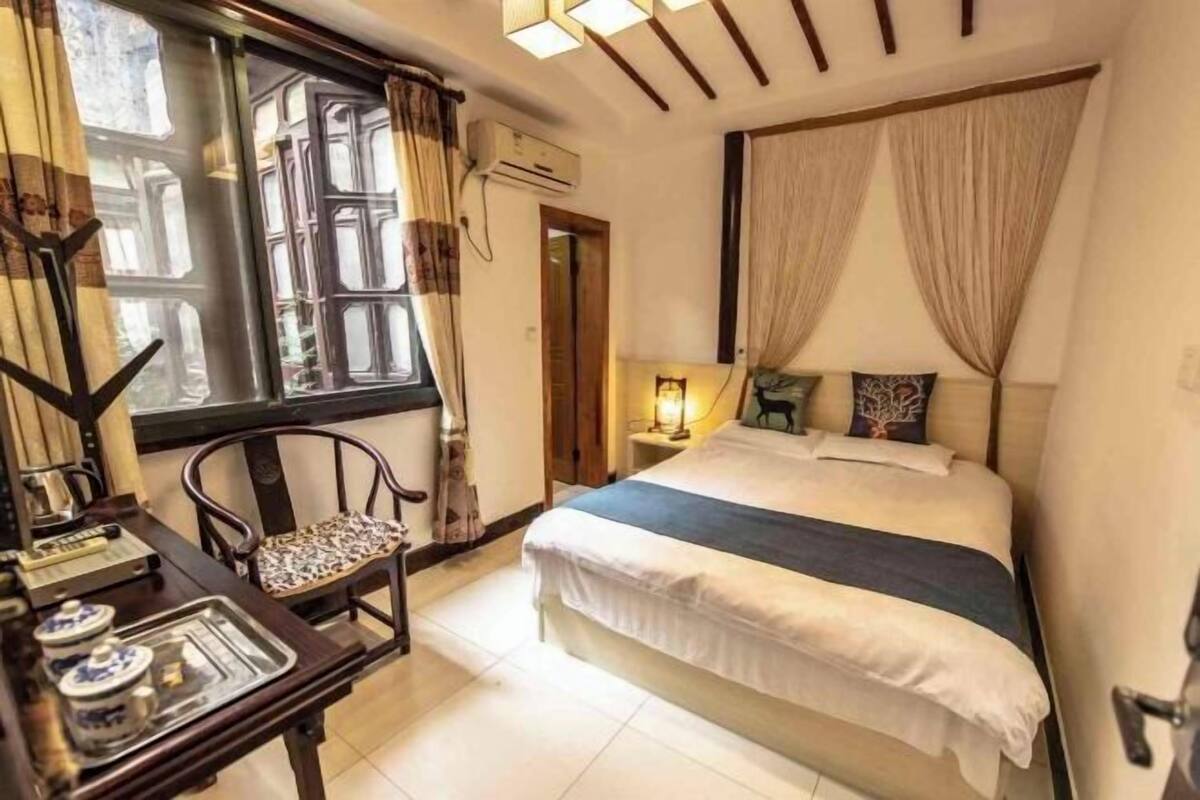 A hotel room with a bed, a desk with a tray, a chair, and a window with curtains.