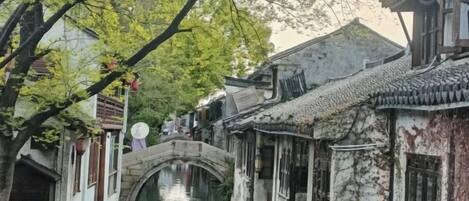 A traditional Chinese courtyard with a stone bridge, narrow waterway, and buildings with tiled roofs.