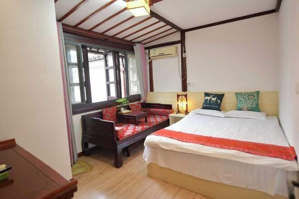 A bedroom with a bed, a sofa, a desk, and a window.