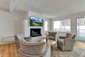Una sala de estar con chimenea, televisor montado encima y vista al exterior a través de amplios ventanales.