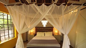 Una cama con dosel, dos lámparas de noche, un ventanal con vistas y un cabecero de madera.