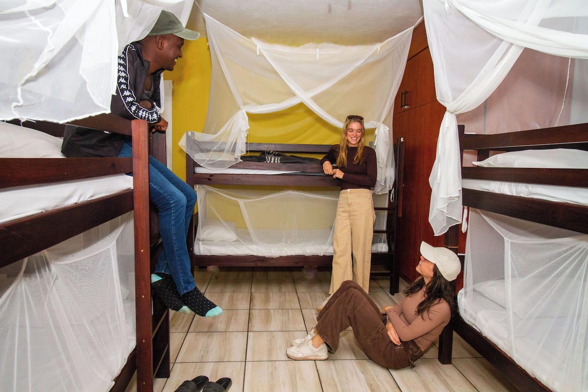 A dormitory room with bunk beds, a bed with a mosquito net, and a small desk.