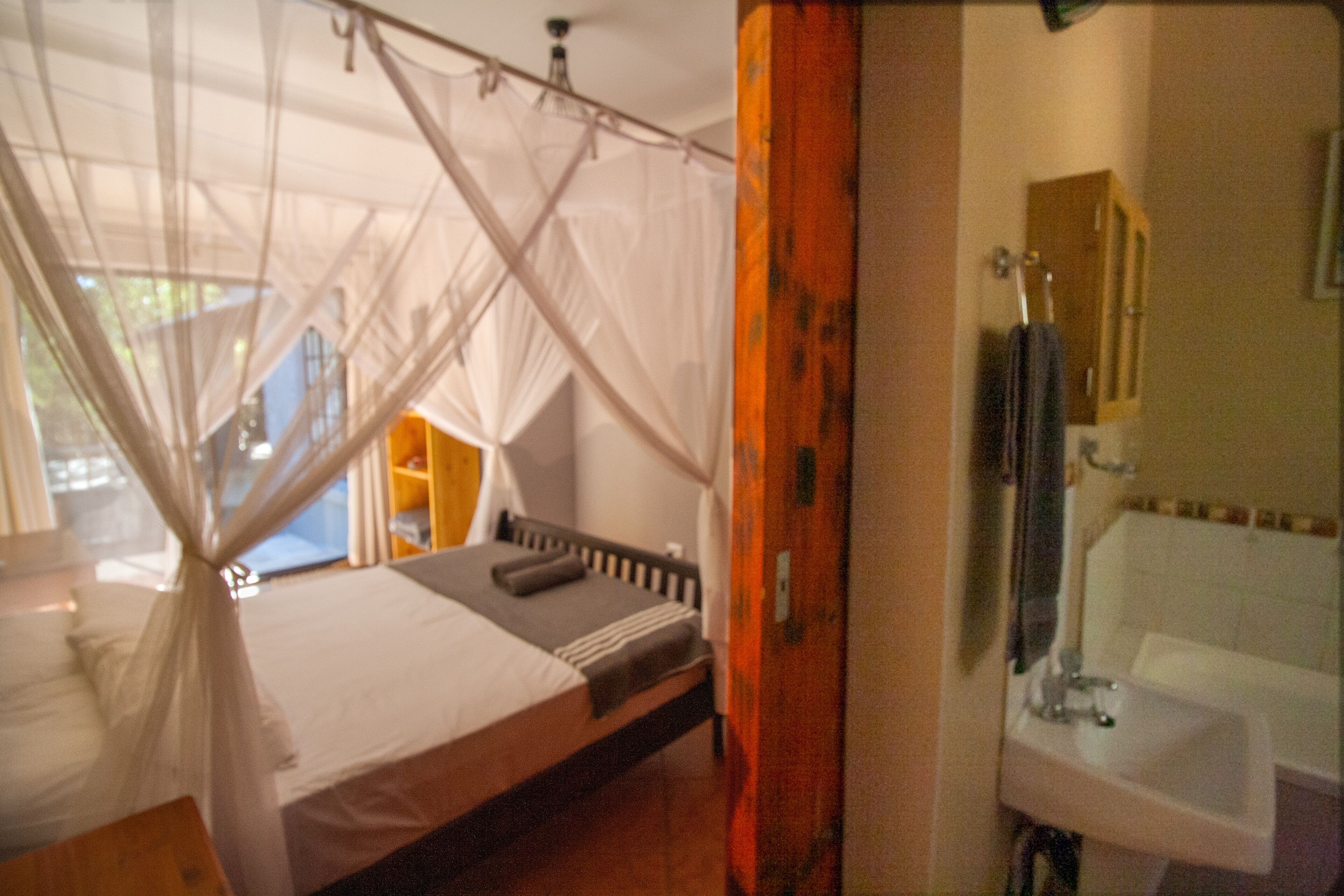 A room with a bed, a window with a view, a bathroom with a sink, and a mirror.