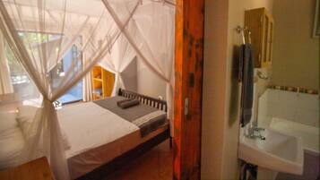 A room with a bed, a window with a view, a bathroom with a sink, and a mirror.
